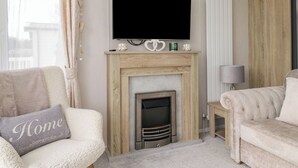 A living room with a fireplace, a television mounted above it, and two sofas. - Swan Haven (Grange-over-Sands)