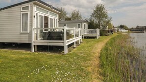 A row of white mobile homes by a lake with a grassy area and a wooden deck. - Swan Haven (Grange-over-Sands)