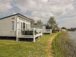 A row of white mobile homes by a lake with a grassy area and a wooden deck. - Swan Haven (Grange-over-Sands)