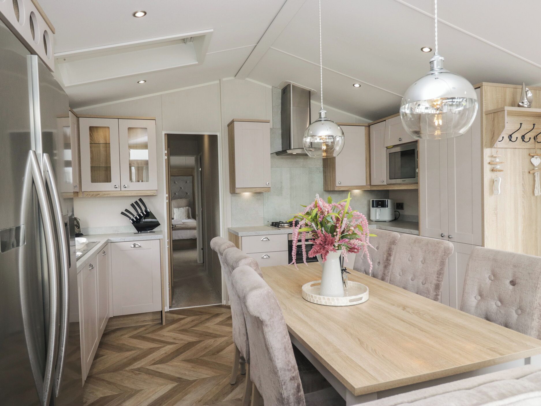 A modern kitchen with a wooden dining table, white cabinets, and pendant lighting.