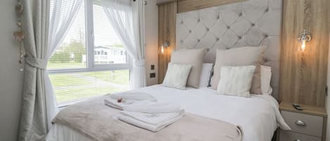 A bedroom with a large bed, a wooden headboard, a bedside table, and a window with curtains.
