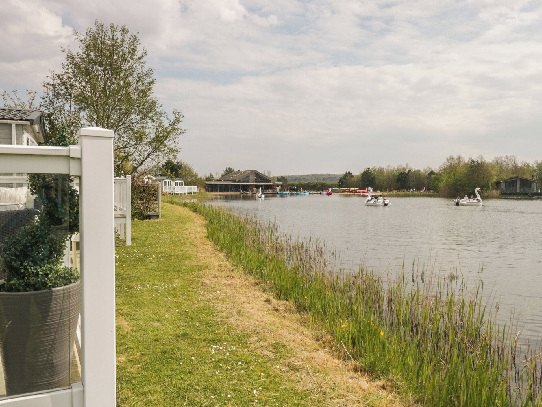 A lakeside view with boats, a grassy path, and buildings in the background.