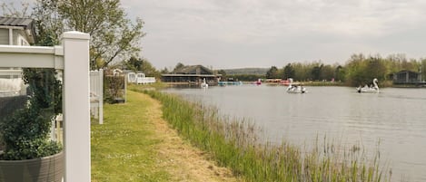 A lakeside view with boats, a grassy path, and buildings in the background.