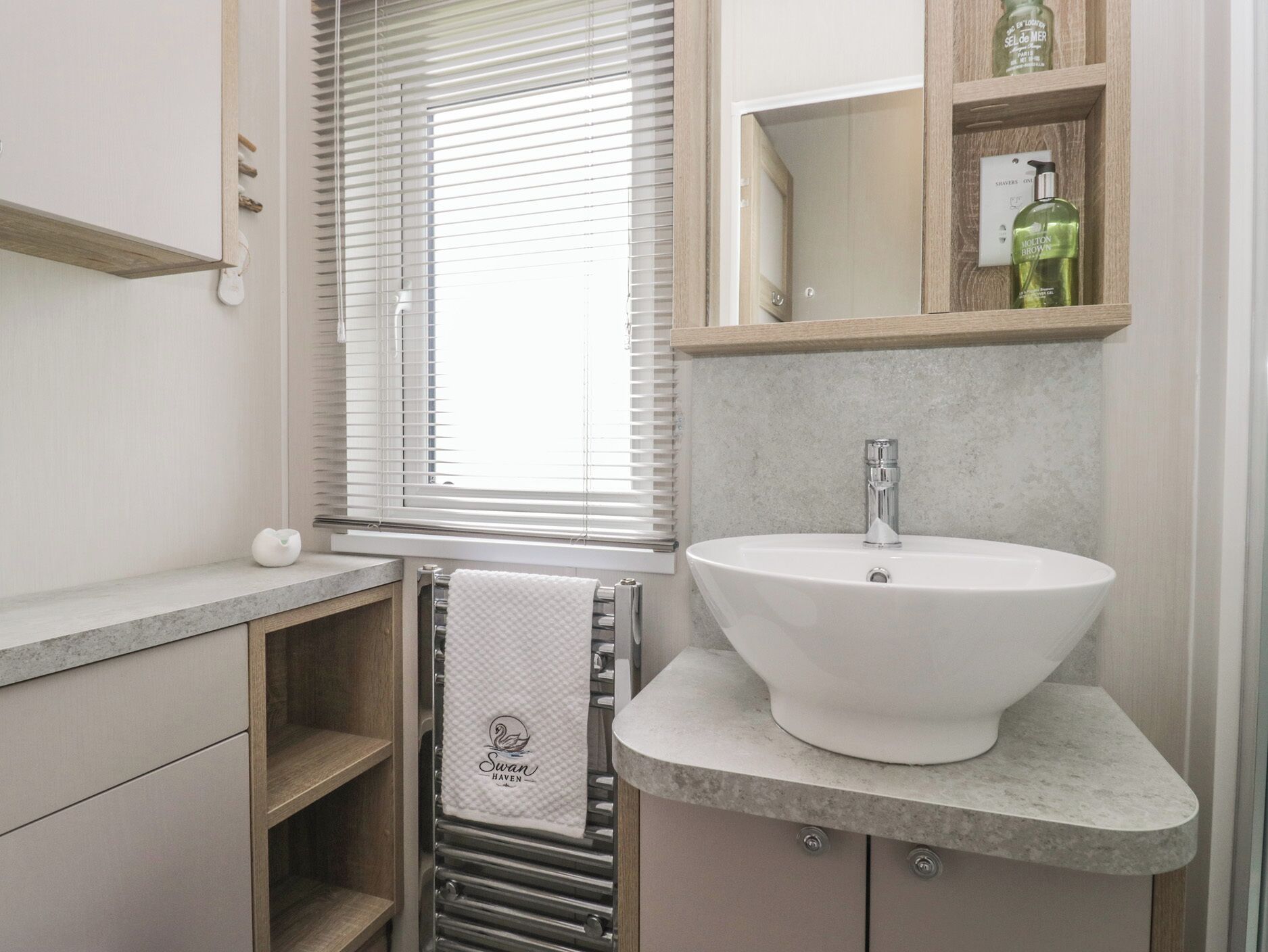 A bathroom with a white sink, a towel rack with a towel, a mirror, and a shelf with toiletries.