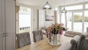 A dining area with a wooden table, grey upholstered chairs, a vase with flowers, and pendant lights. - Swan Haven (Grange-over-Sands)