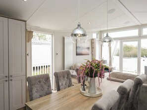 A dining area with a wooden table, grey upholstered chairs, a vase with flowers, and pendant lights. - Swan Haven (Grange-over-Sands)