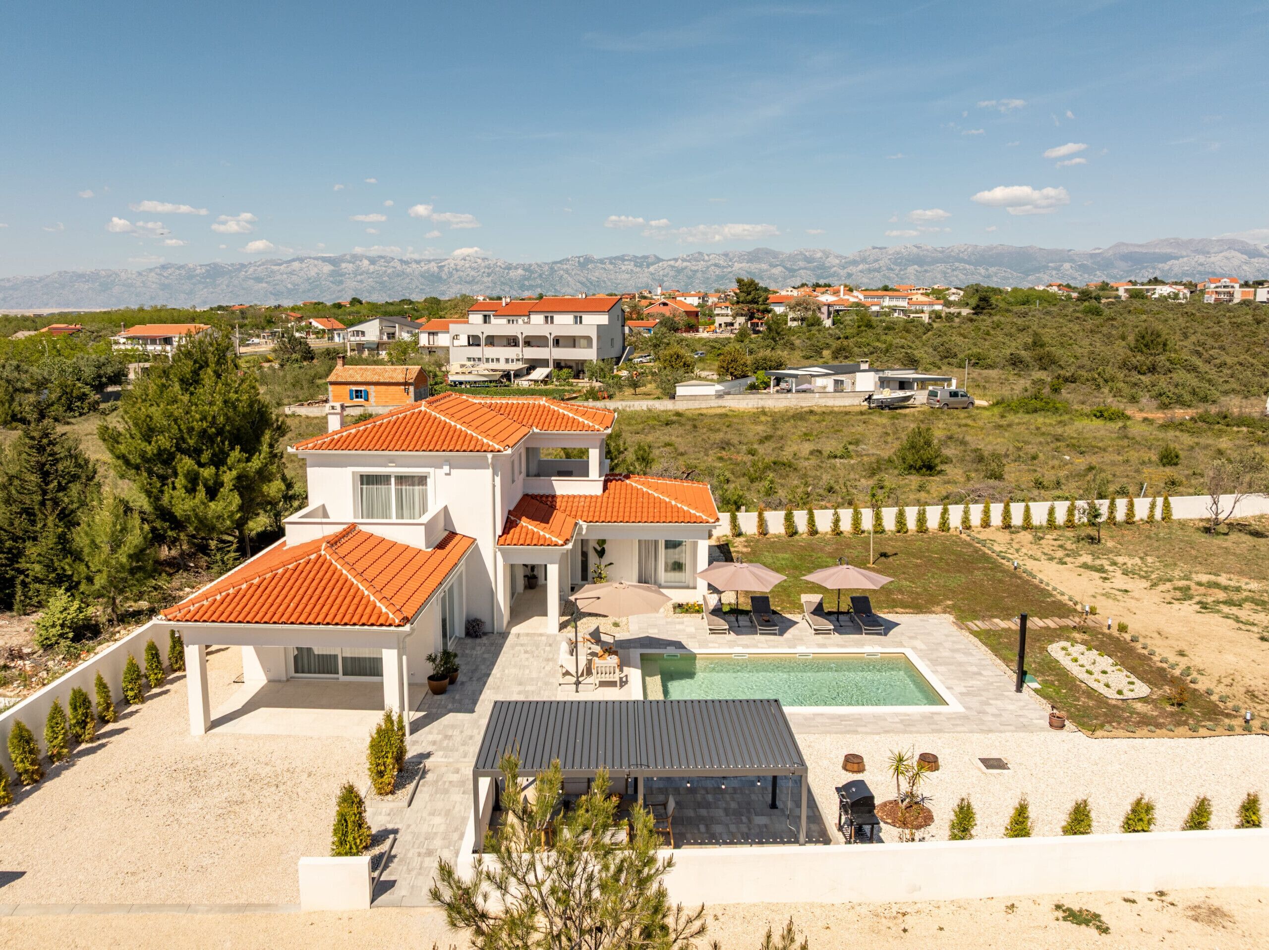 En modern villa med en swimmingpool, utomhusmöbler och utsikt över det omgivande landskapet.