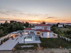 Ein modernes, zweistöckiges Haus mit Swimmingpool, umgeben von einem gepflegten Garten und Blick auf den Sonnenuntergang.