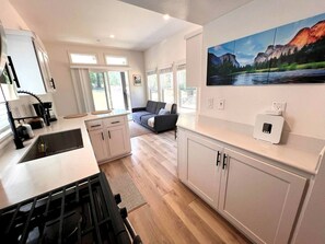 Eine moderne Küche mit weißen Schränken, einem eingebauten Herd und einem Essbereich mit einer grauen Couch.