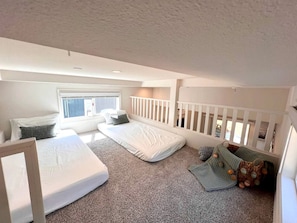 Ein Schlafzimmer mit zwei Betten, einem Babybett, einem Fenster und einem Balkon.
