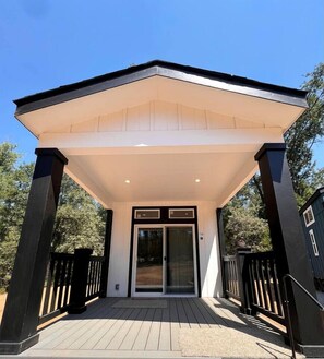 Un espace extérieur abrité doté d’une terrasse en bois, d’une entrée avec porte vitrée et d’un bâtiment de couleur sombre en arrière-plan.