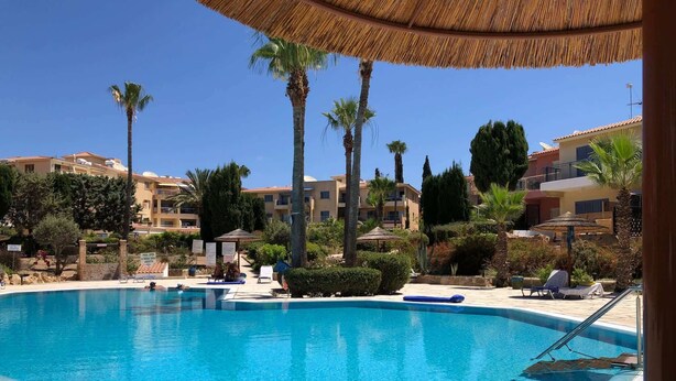 Una piscina con sillas de descanso y sombrillas, rodeada de palmeras y edificios.