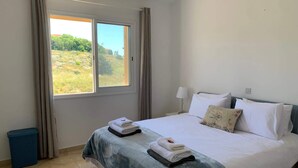 Un dormitorio con cama, ventana con cortinas, lámpara de noche y vistas a zonas verdes.