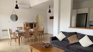 Una sala de estar con un sofá, una mesa de centro de madera, una mesa de comedor con sillas y una zona de cocina con armarios y un refrigerador.