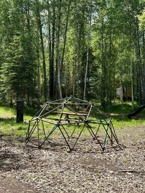 Una estructura de domo geodésico en una zona boscosa, con una mesa de picnic cerca.