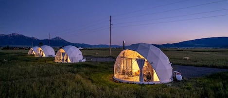 Geodesic dome tents in a grassy field with mountains in the background.
