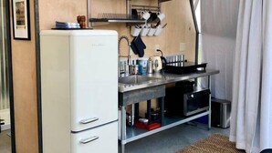 A compact kitchen with a white refrigerator, a sink, and a stove. There are shelves above the counter holding dishes and glasses. A black chair is visible in the foreground. - Secluded Montana Dome Retreat with Stunning Mountain Views Near Yellowstone National Park (Park County)