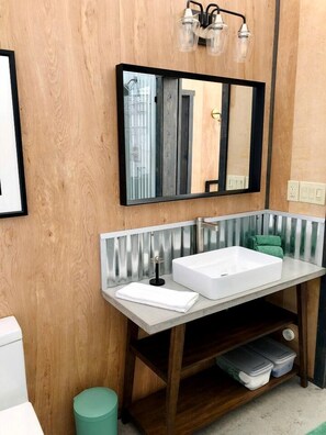 Un baño moderno con tocador de madera, un espejo grande y una lámpara de pared.