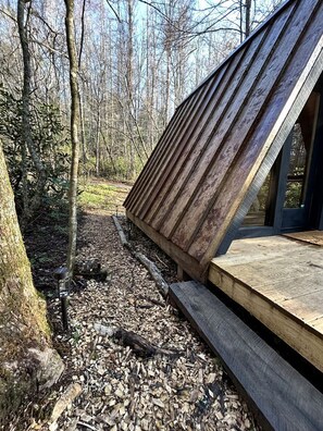 A wooden deck with a sloped roof, surrounded by trees and a forested area. - Secluded Off-Grid Cabin Retreat with Fire Pit & Sauna in Zirconia, North Carolina (Zirconia)
