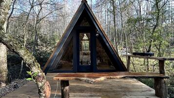 A wooden deck with a triangular wooden structure, possibly a gazebo or shelter, surrounded by trees.