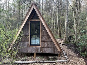 A small, triangular wooden cabin with a large window, surrounded by a forest. - Secluded Off-Grid Cabin Retreat with Fire Pit & Sauna in Zirconia, North Carolina (Zirconia)