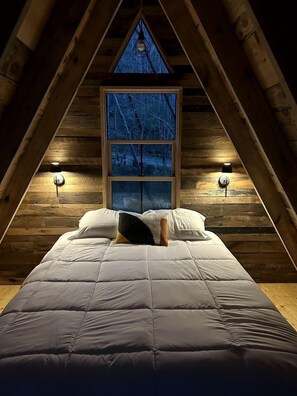 Un dormitorio con una cama, una ventana y dos lámparas fijadas a la pared.