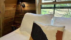Ein Bett mit weißen Leinen und einem einzelnen Zierkissen in einem Blockhaus mit Holzwänden und einem Fenster.