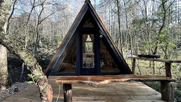 A wooden deck with a triangular wooden structure, possibly a gazebo or shelter, surrounded by trees.