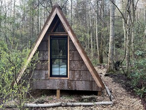 A small, triangular wooden cabin with a large window, surrounded by a forest. - Secluded Off-Grid Cabin Retreat with Fire Pit & Sauna in Zirconia, North Carolina (Zirconia)