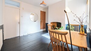 A room with a wooden dining table, chairs, a round mirror, and a hanging pendant light. - Victorian Terrace Near Uni, Sleeps 6, Garden (Reading)