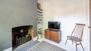 A living room with a fireplace, a TV on a wooden cabinet, a wooden chair, and a plant. - Victorian Terrace Near Uni, Sleeps 6, Garden (Reading)