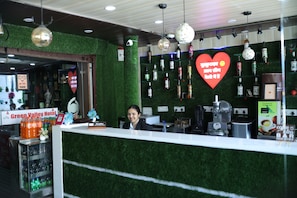 Zona de recepción de hotel con una pared verde, un letrero con forma de corazón y una variedad de botellas de licor en estantes.