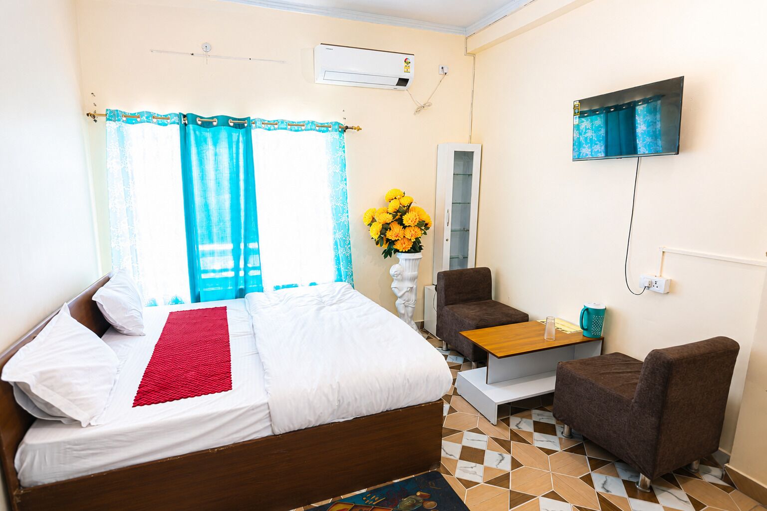 A hotel room with a bed, a small table, a chair, a TV, and a window with curtains.
