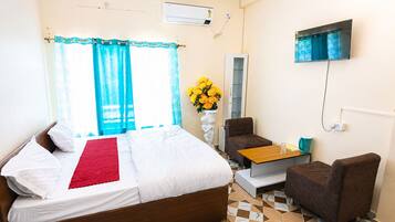 A hotel room with a bed, a small table, a chair, a TV, and a window with curtains.