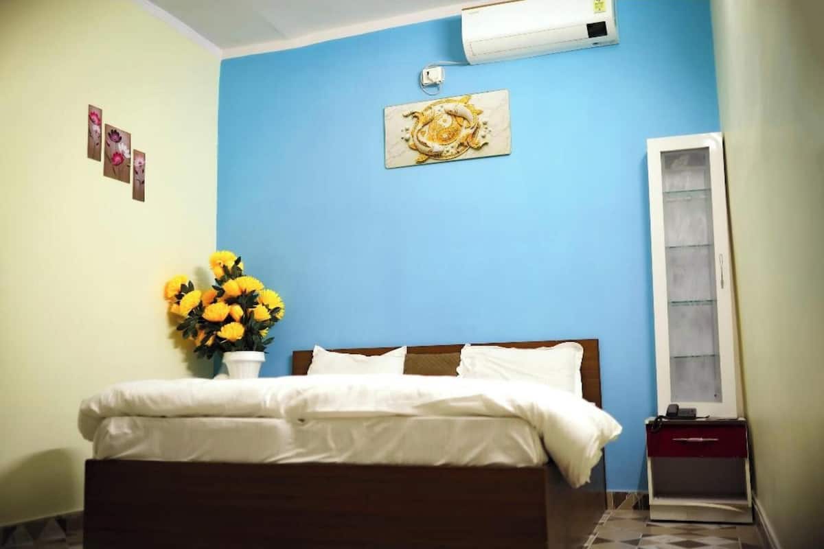 Een slaapkamer met een bed, een luchtverkoeler aan de muur, een vaas met gele bloemen en een spiegel.