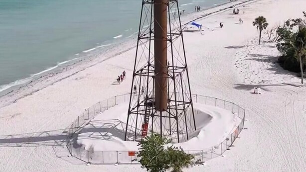A beach with a lighthouse, palm trees, and a sandy shore.