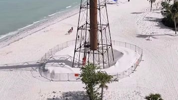 A beach with a lighthouse, palm trees, and a clear sky.