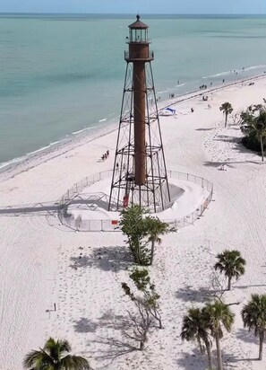 Una playa con un faro, palmeras y cielo despejado.