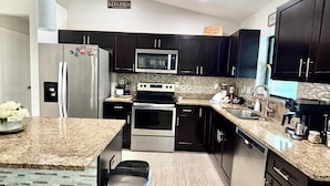 A modern kitchen with granite countertops, stainless steel appliances, and dark cabinetry.