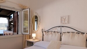 Ein Schlafzimmer mit einem Bett, einem Nachttisch mit Lampe, einem Fenster mit Rollläden, einem Spiegel und einer Wanddekoration.