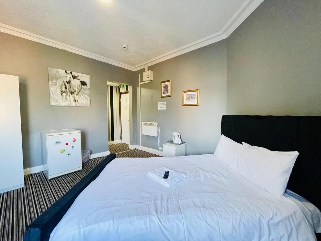 Une chambre d’hôtel avec un grand lit, un petit bureau, un réfrigérateur, une porte et un tableau accroché au mur.