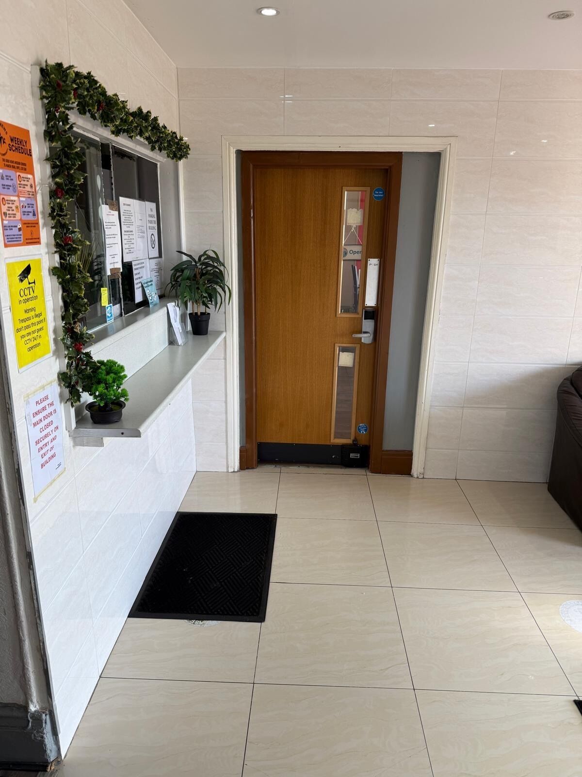A reception area with a wooden door, a reception desk, and a black mat on the floor.