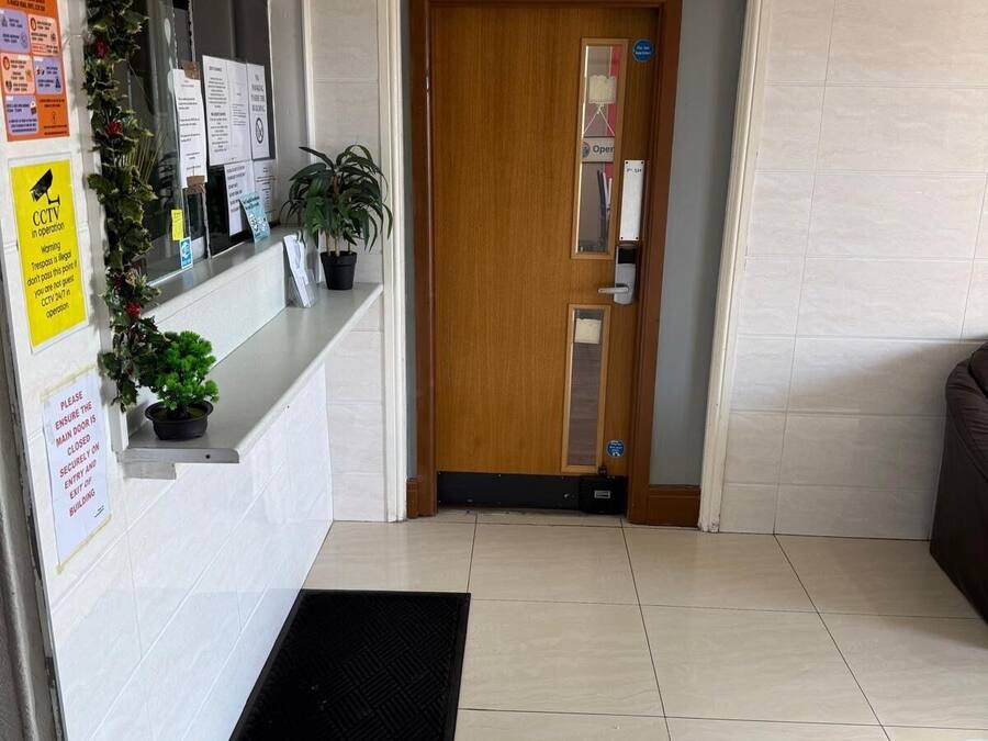 A reception area with a wooden door, a reception desk, and a black mat on the floor.