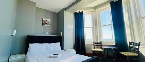 A hotel room with a bed, a desk, and a chair. There is a window with curtains.