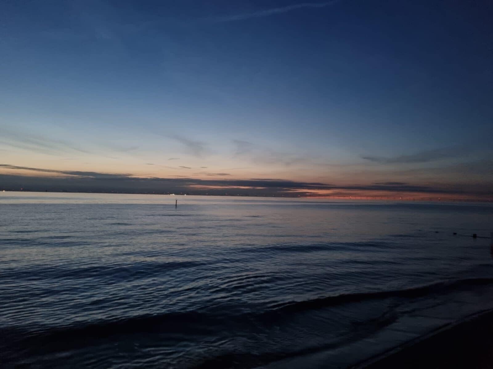 A calm sea with a clear horizon and a single buoy in the distance.