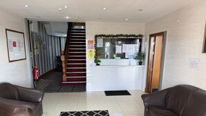 A hotel lobby with a reception desk, a staircase, two leather sofas, a patterned rug, and a fire extinguisher.