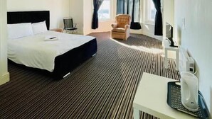 A hotel room with a bed, a chair, a desk, and a window with curtains.
