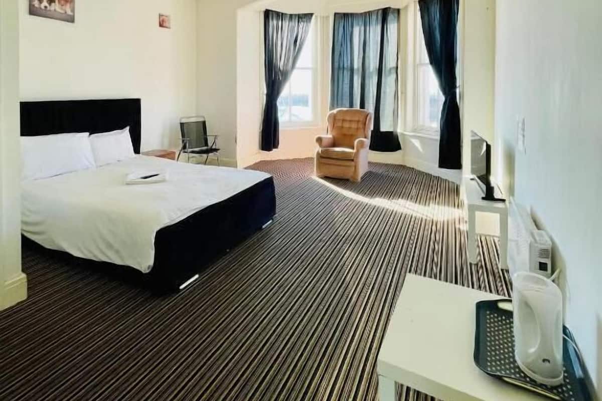 A hotel room with a bed, a chair, a desk, and a window with curtains.