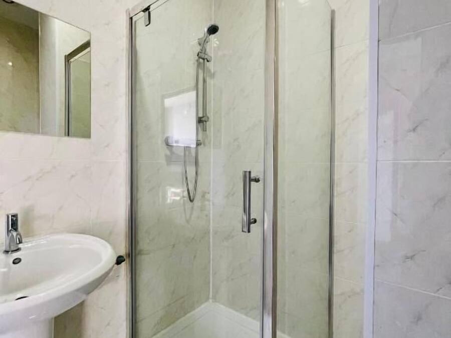 A bathroom with a glass-enclosed shower, a sink, and a mirror.
