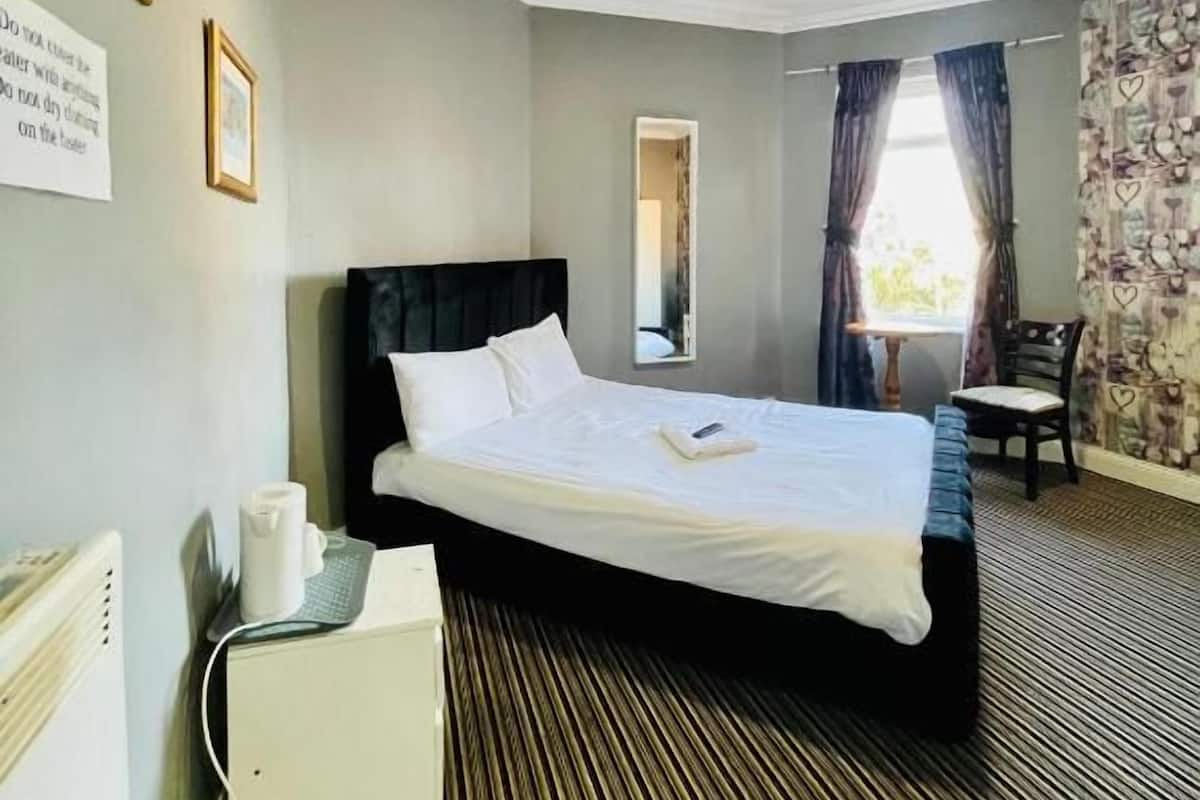 A hotel room with a bed, a desk with a computer, a chair, and a window with curtains.